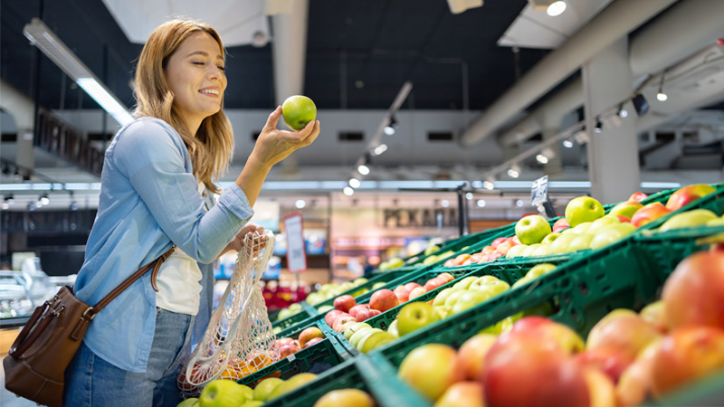donna davanti al banco della frutta con mela in mano